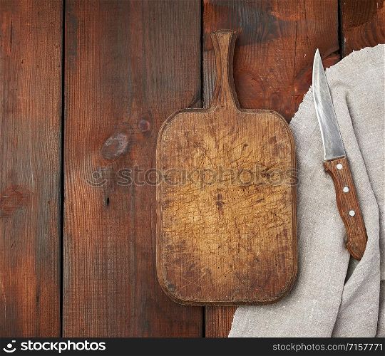 very old empty wooden rectangular cutting board and knife, top view, brown wooden background
