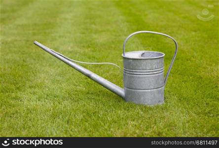 Very old metal watering-can on a green field