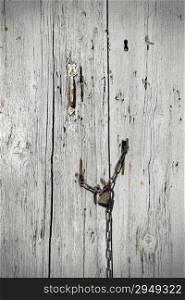 Very old wooden door with handle and padlock hanging on the chain