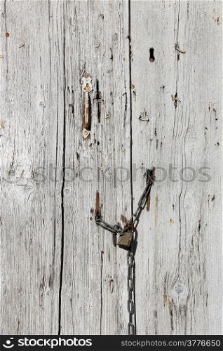 Very old wooden door with handle and padlock hanging on the chain