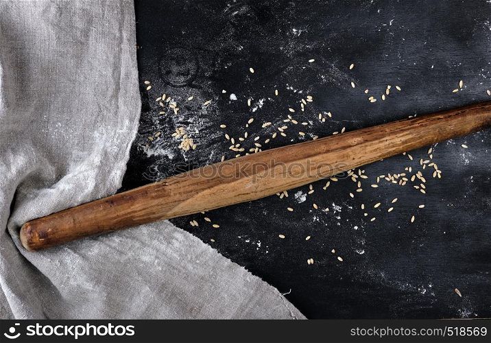 very old wooden rolling pin on a black background, near a gray linen towel, top view, sprinkled with flour and wheat