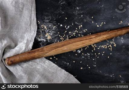 very old wooden rolling pin on a black background, near a gray linen towel, top view, sprinkled with flour and wheat