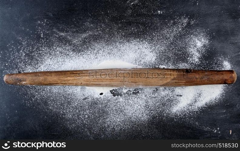 very old wooden rolling pin on a black background, top view, scattered white wheat flour