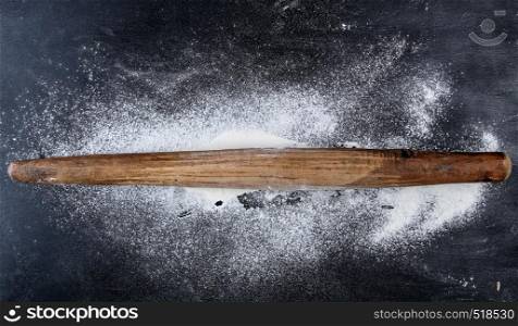 very old wooden rolling pin on a black background, top view, scattered white wheat flour