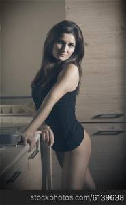 very pretty brunette woman with long hair, nude legs and sexy black undershirt in sensual pose in kitchen looking in camera