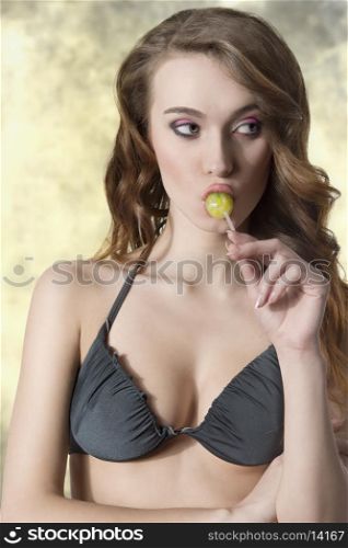 very pretty girl with summer style and long wavy hair wearing bikini and eating lollipop
