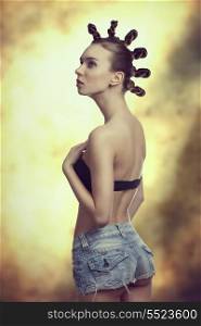 very pretty woman posing with creative hairstyle, sexy denim shorts and bra, showing her back and looking up