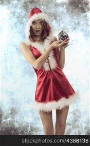 very pretty woman with christmas style wearing short red xmas dress and fur hood. Showing the bauble in her hands with happy expression
