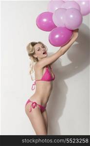very pretty young girl with blonde hair-style and sexy bikini playing with pink balloons in summertime
