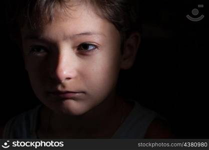 very sad boy in the dark, focused light on the one side, looking away