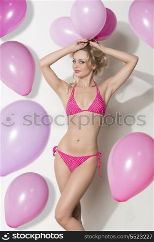 very sexy blonde woman with bikini taking pink balloons on her head and looking in camera.