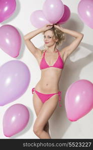 very sexy blonde woman with bikini taking pink balloons on her head and looking in camera.