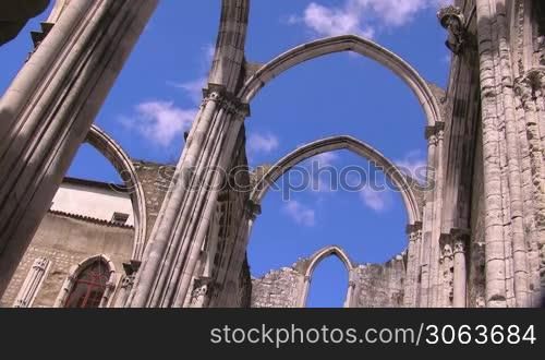 Verzierte Rundbogen / Tore aus Stein einer alten Kathedrale; im Hintergrund das Gebaude der Kathedrale; wei?e Wolken ziehen am blauen Himmel.