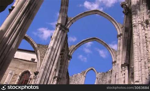 Verzierte Rundbogen / Tore aus Stein einer alten Kathedrale; im Hintergrund das Gebaude der Kathedrale; wei?e Wolken ziehen am blauen Himmel.