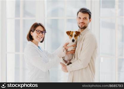 Vetarinary and animal healthcare concept. Happy smiling female vet care about dogs health, going to examine jack russell terrier, talks with client, works in medical center for domestic animals