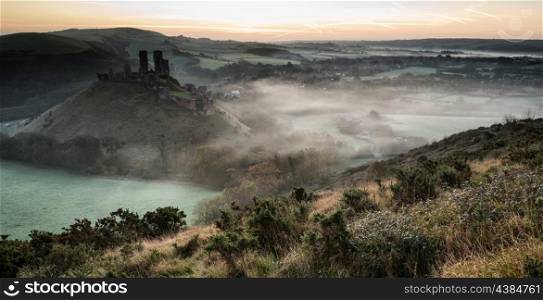 Vibrant sunrise over medieval castle ruins with fog in rural landscape