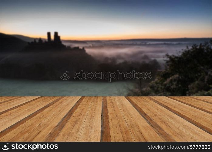 Vibrant sunrise over medieval castle ruins with fog in rural landscape with wooden planks floor