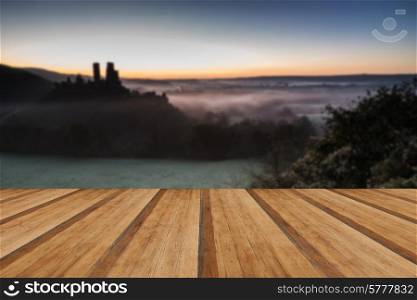 Vibrant sunrise over medieval castle ruins with fog in rural landscape with wooden planks floor