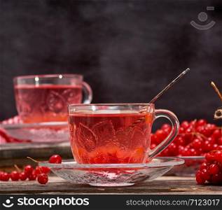 viburnum tea in a transparent cup with a handle and saucer on a gray wooden table, next to fresh berries