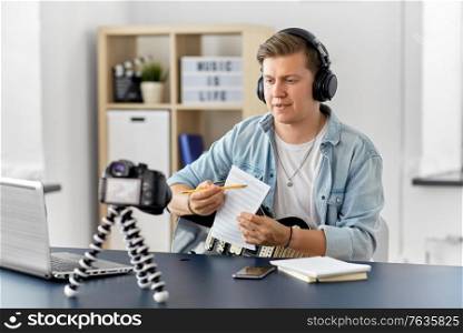 video blogging and people concept - young man or musician in headphones with camera, music book and guitar videoblogging at home. man or blogger with camera, music book and guitar