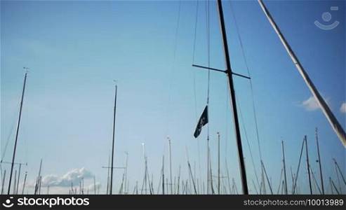 A lot of masts are swinging in a harbor, a pirate flag on one mast is focused