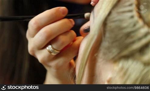 A makeup artist is using a brush to apply makeup to an attractive young woman's eyelids