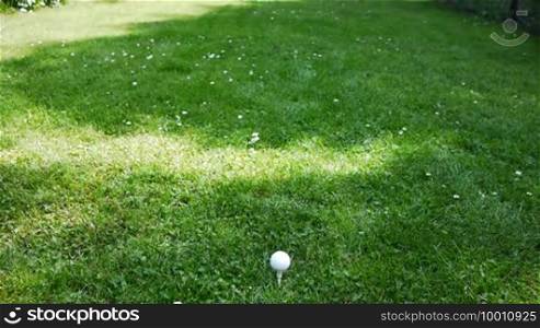 A man aims with the golf club at a golf ball and hits it, the ball flies.
