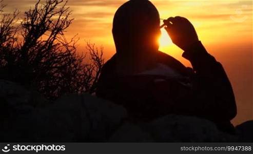 A man is watching a blazing yellow sunset, looking towards the sun, creating only a silhouette