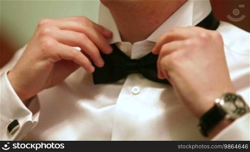 A man puts on a bow tie