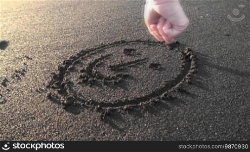 A smiley is being painted in the sand.
