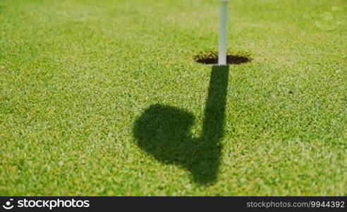 A strong shadow or drop shadow of a target flag in a golf hole is visible in the blowing wind - suitable for metaphors like last shot is overshadowed, etc.