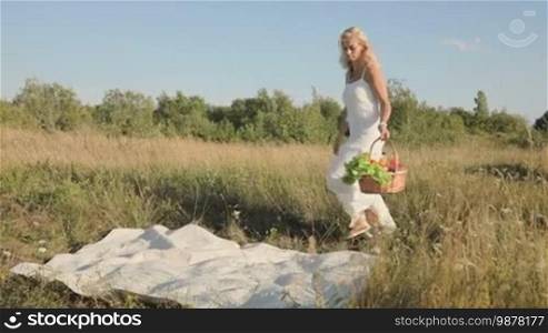 A woman carries food in a basket and puts them on a blanket in nature at sunset. Slow motion.