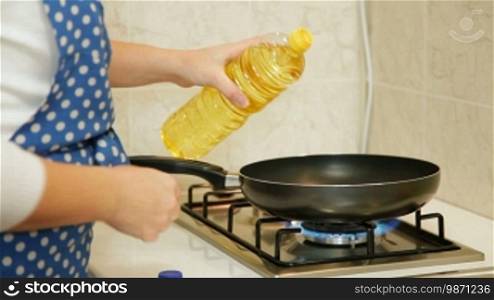 A woman preparing food at home, pouring olive oil into frying pan