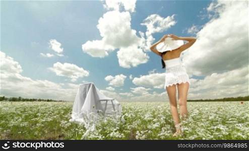A young woman in a white hat relaxing on a white blossoming meadow looking at the camera