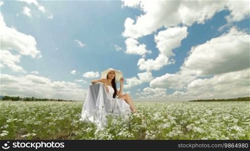 A young woman in a white hat relaxing on a white blossoming meadow