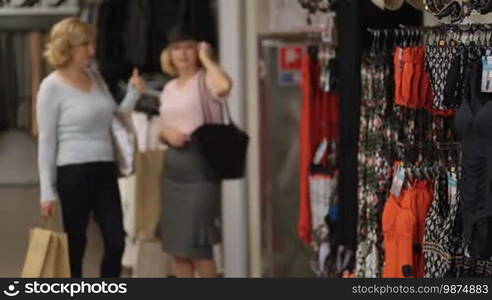 Active elderly females enjoying leisure together while shopping in clothing store during sale season. Senior women with shopping bags buying clothes to renew wardrobe in fashion shop. Women in holiday shop choosing swimsuits and summer accessories