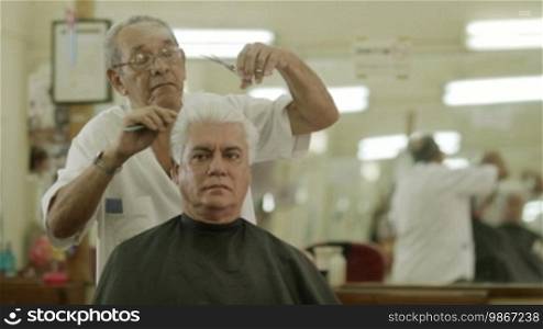 Active retired old people, man getting a haircut by senior barber in old-fashioned barber's shop or male beauty parlor