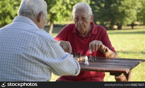Active retired people, old friends and free time, two senior men having fun and playing chess at park. Sequence of medium and wide shot