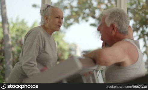 Active retired people, old man and woman talking and exercising in fitness gym