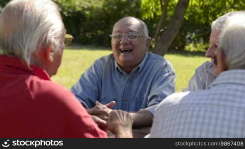 Active retired senior people, old friends and leisure, group of four elderly men having fun, laughing and talking in city park. Sequence of medium and wide shots