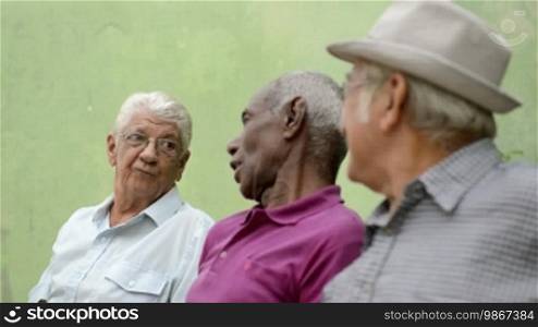 Active retirement and senior people, group of three elderly male friends talking and laughing on a bench in a public park. Sequence