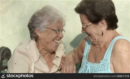 Active retirement, two elderly female friends talking and laughing on a bench in a public park