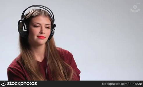 Adorable brunette girl wearing red lipstick and enjoying the track on the radio with headphones. Sexy young woman with long hair looking at the camera playfully and seductively touching her red lips with finger while listening music in earphones.