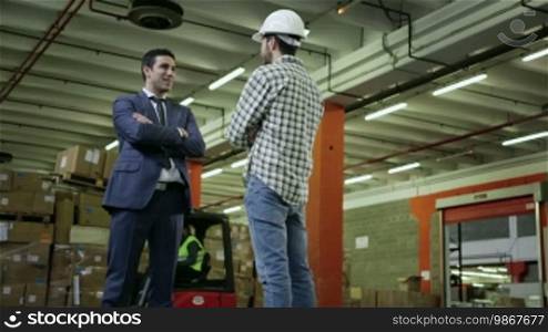 Adult business man in logistics facility talking to manual worker, staff people working in warehouse, men in industry. 1 of 19