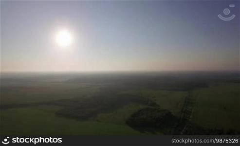 Aerial high level flight above the agricultural fields with green grass and forests in day time at summer against horizon, Russia