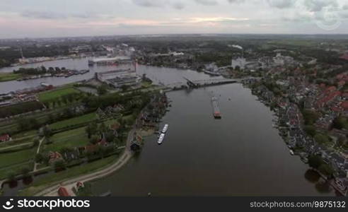 Aerial panorama of town in Netherlands. Private houses, green areas and river with sailing barge