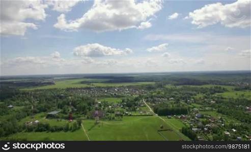 Aerial panorama of vast green areas in Russia. Summer landscape with forests, fields, village and blue cloudy sky