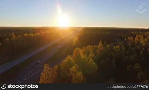 Aerial panoramic of a highway with traffic among a mixed hardwoods and conifer forest at sunset