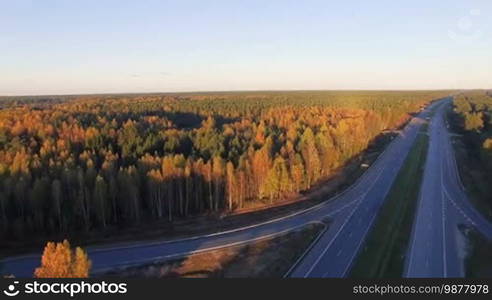 Aerial panoramic of a highway with traffic among a mixed hardwoods and conifer forest at sunset