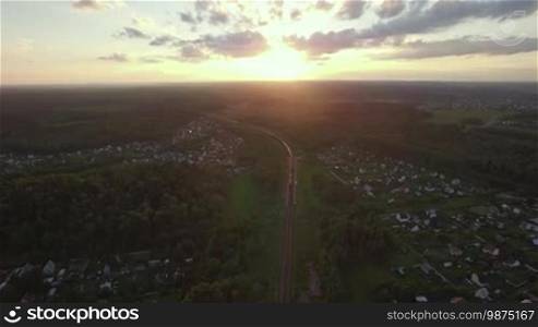 Aerial rural scene with village and freight train running through it at sunset, Russia